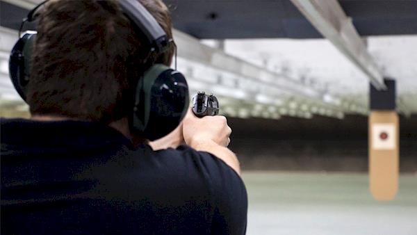 Looking Over the Right Shoulder of a Shooter Shooting at an Indoor Range at a Paper Target